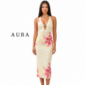 A woman modeling a sleeveless halter midi dress with a cream base and pink floral print, shown against a plain white background with the brand name AURA on the left.