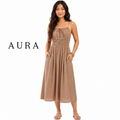 A woman modeling a sleeveless midi dress in a warm taupe-brown color, featuring a gathered smocked bodice, thin straps, and side pockets. The brand name 'AURA' is printed in black text on the left side of the image, set against a plain white background.