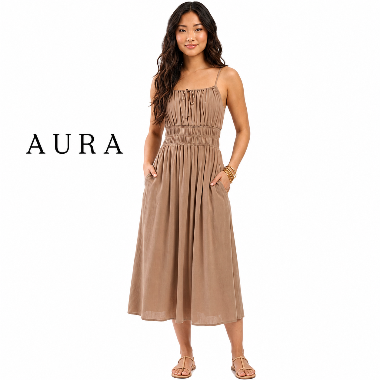 A woman modeling a sleeveless midi dress in a warm taupe-brown color, featuring a gathered smocked bodice, thin straps, and side pockets. The brand name 'AURA' is printed in black text on the left side of the image, set against a plain white background.