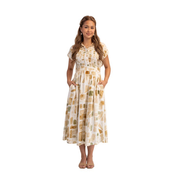 A woman modeling a short-sleeve midi dress with a beige, brown, and muted green abstract block pattern on a white background. The brand name 'AURA' is printed in black text on the right side of the image.